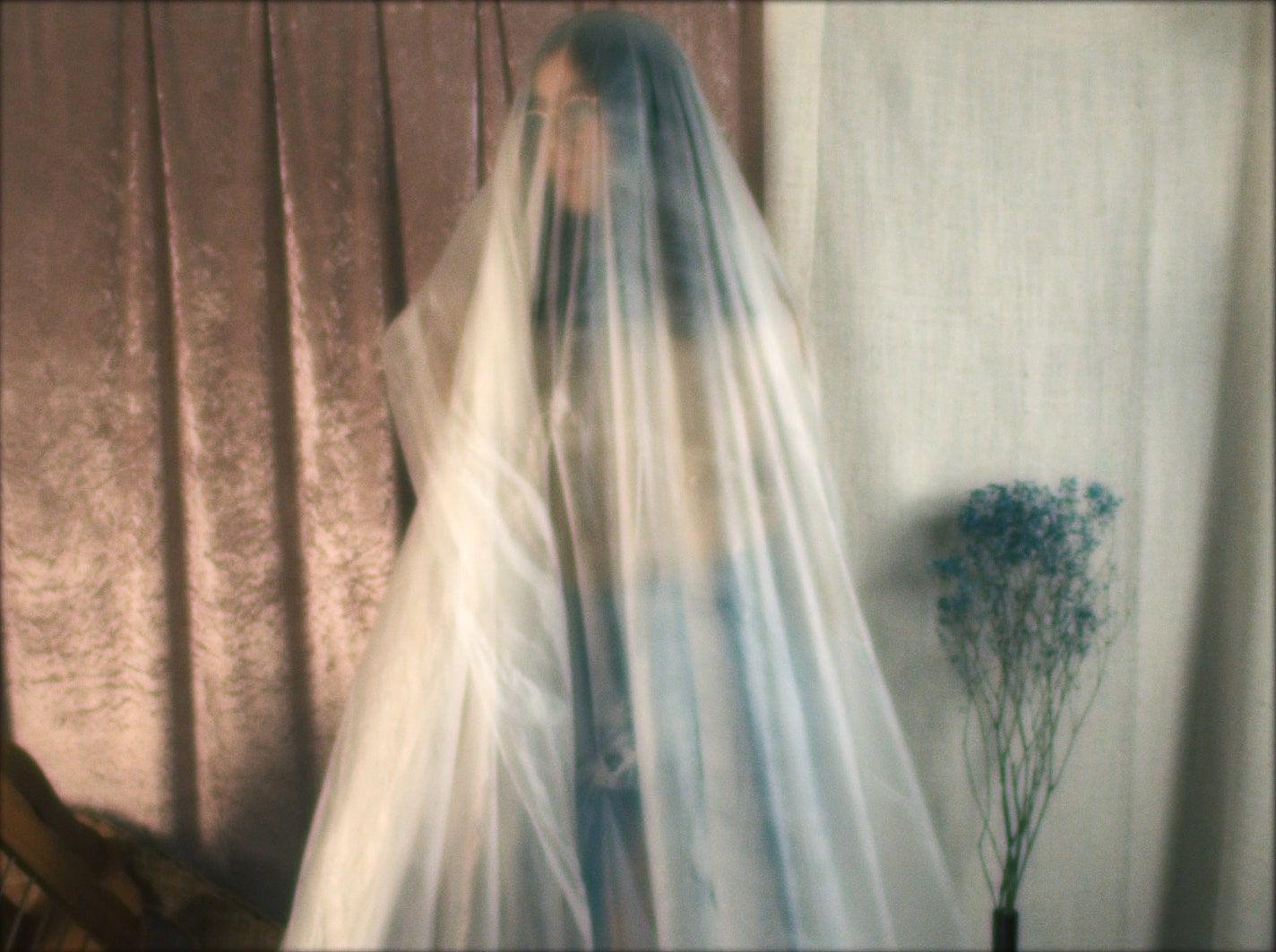 Shrowded in a plastic sheet, a woman gazes out of frame